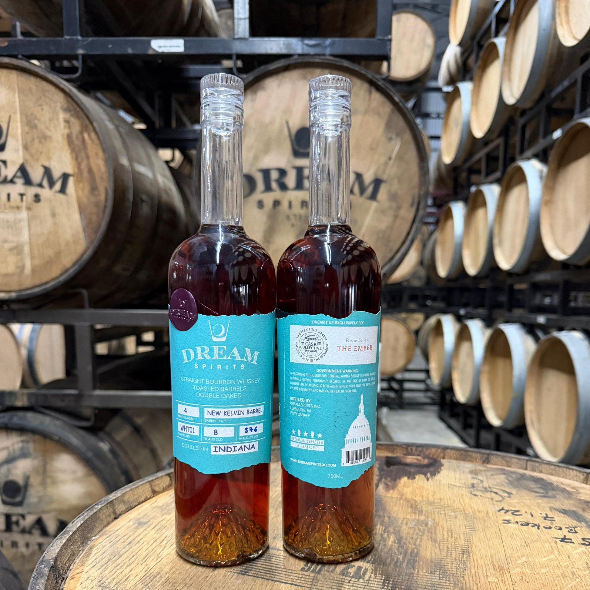 Two bottles of Dream Spirits whiskey on a wooden barrel with barrels in the background.